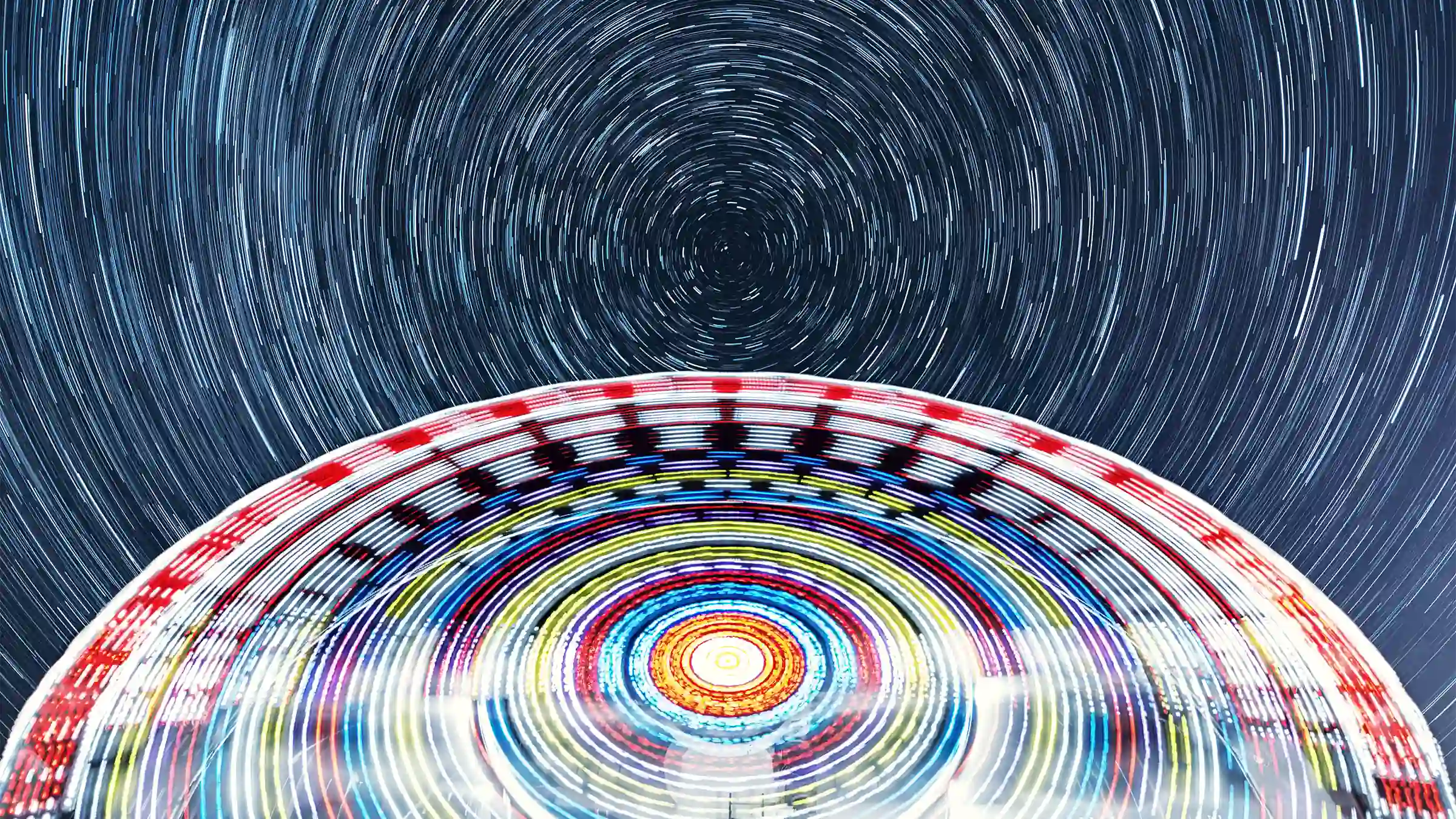 swirly ferris wheel shot from below, and a starry long exposure night sky, also swirly in a circle, mirroring the wheel