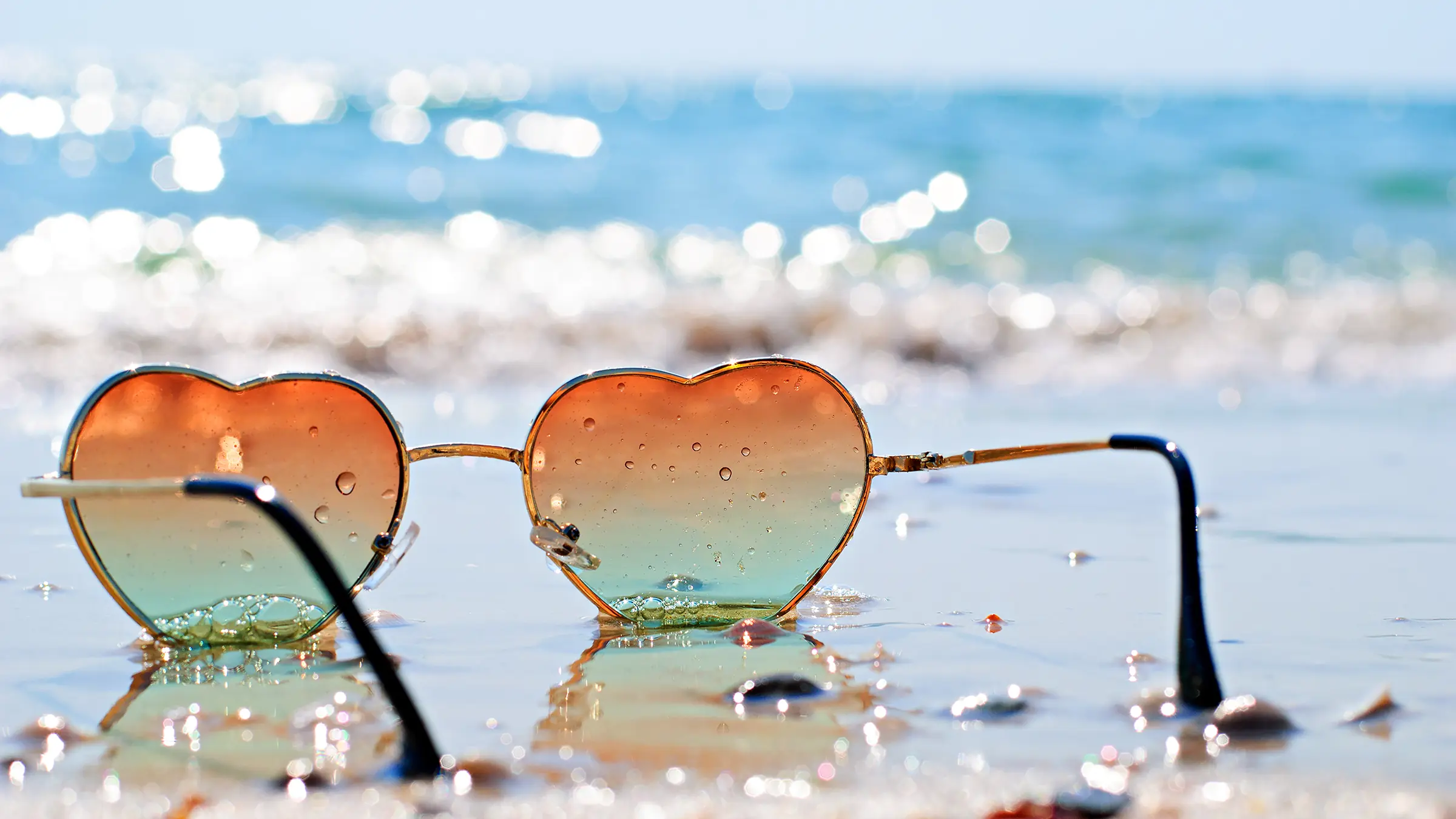 heart-shaped and rose-colored sunglasses, sitting on a sandy beach